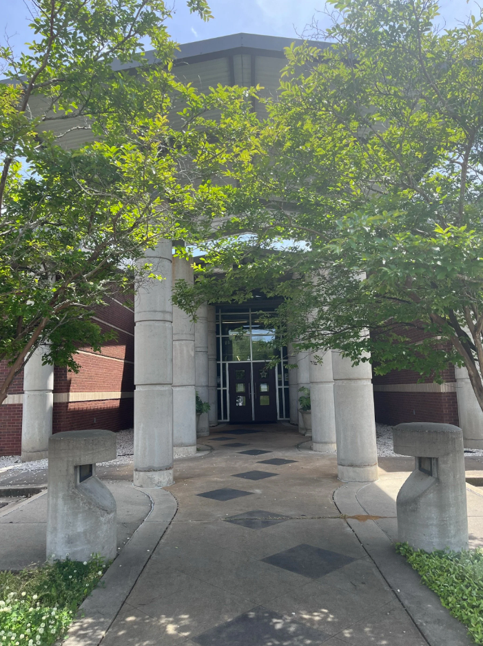 Entryway of Brandon Public Library with large concrete columns, glass doors, brick and concrete facade, and shaded trees lining the pathway.