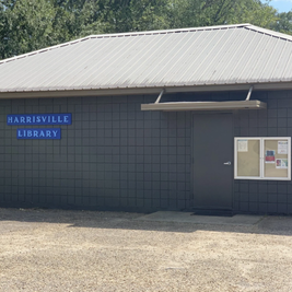 Harrisville Public Library with gray facade, metal roof, and bulletin board near entrance.