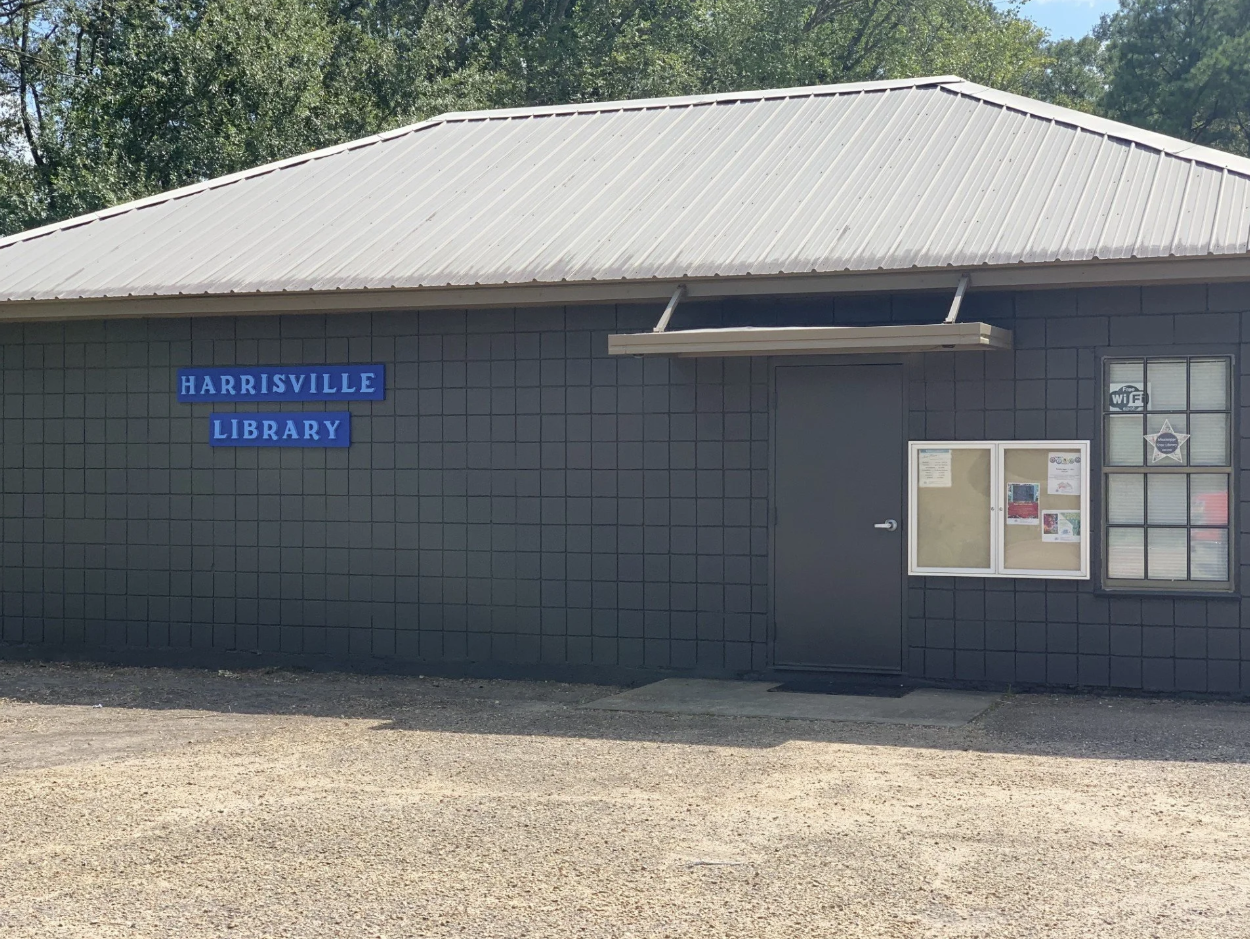 Harrisville Public Library with gray facade, metal roof, and bulletin board near entrance.