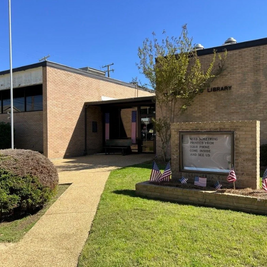 Magee Public Library with brick exterior, patriotic signs, and American flags near entrance.