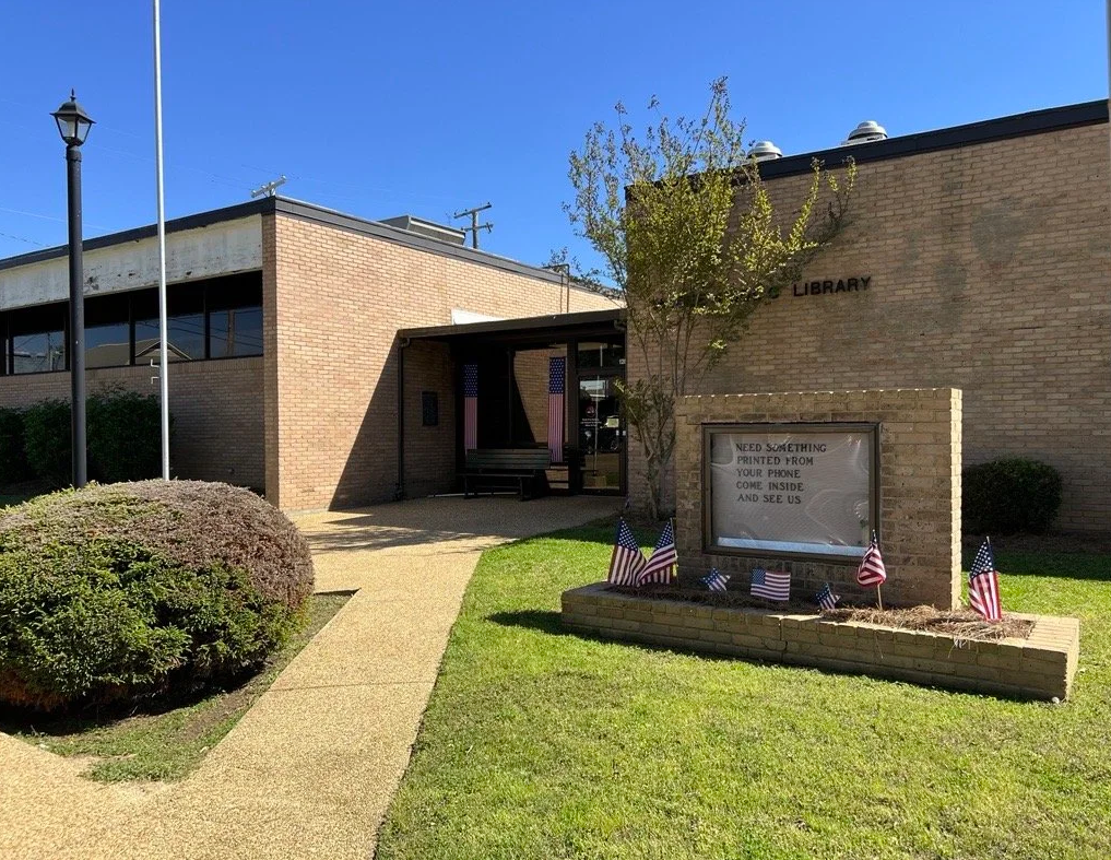 Magee Public Library with brick exterior, patriotic signs, and American flags near entrance.