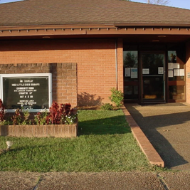 Mendenhall Public Library with red brick exterior, glass entrance, and event sign near walkway.