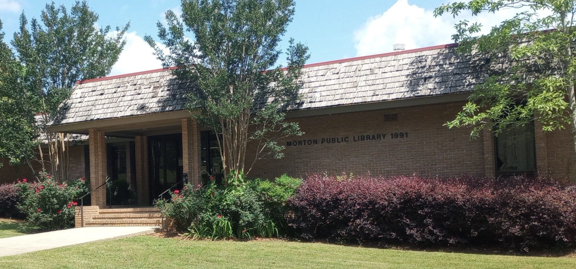 Morton Public Library with brick facade, shingled roof, and landscaped entrance.