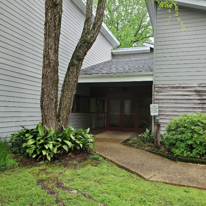 Northwest Point Reservoir Library entrance with gray siding, covered walkway, and surrounding greenery.