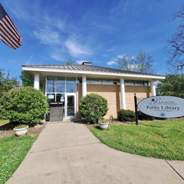 Point Reservoir Library with gray siding, tree in foreground, and pathway leading to entrance.