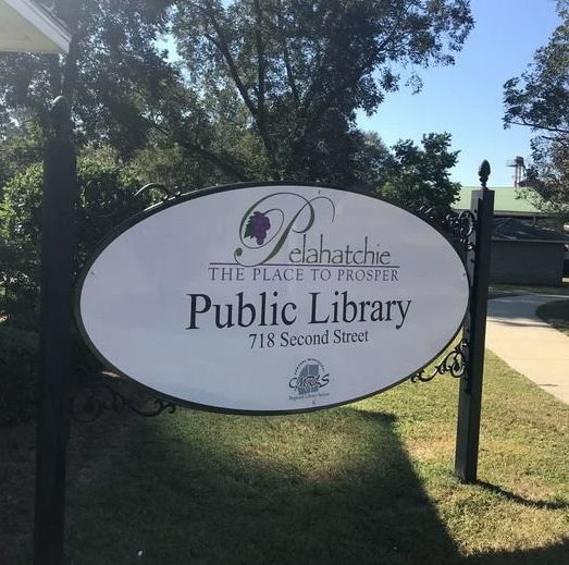  Sign for Pelahatchie Public Library reading mounted on decorative black posts with trees and sidewalk in the background.