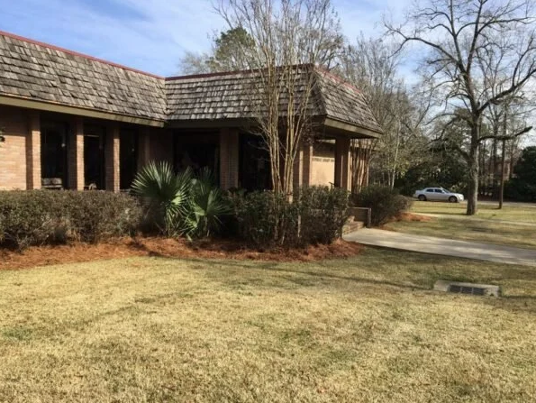 Exterior of Sebastopol Public Library, a brick building with a shingled roof, surrounded by shrubs and trees, with a concrete walkway leading to the entrance.