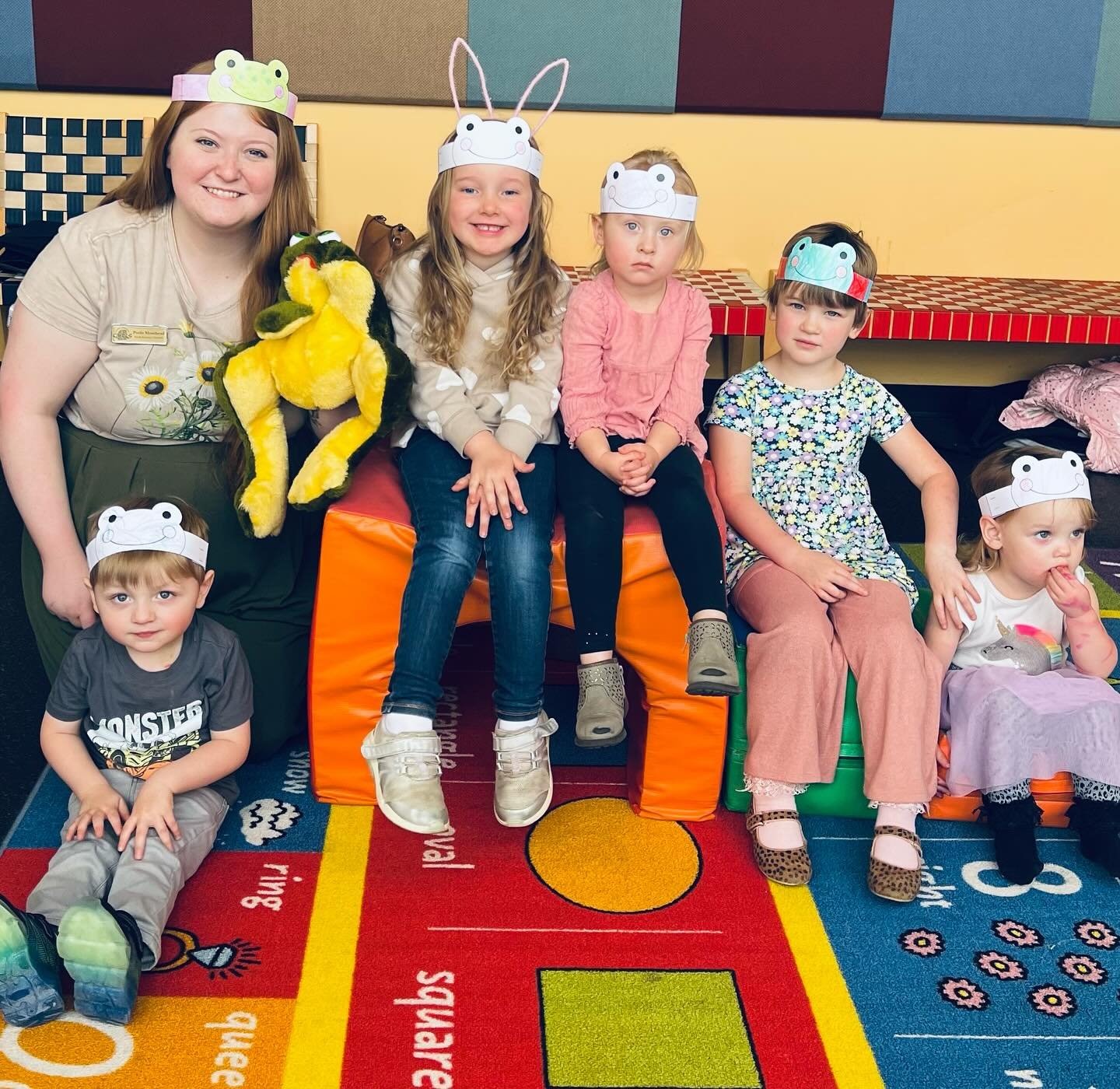 Six people sitting on colorful blocks and carpet, wearing animal-themed headbands.