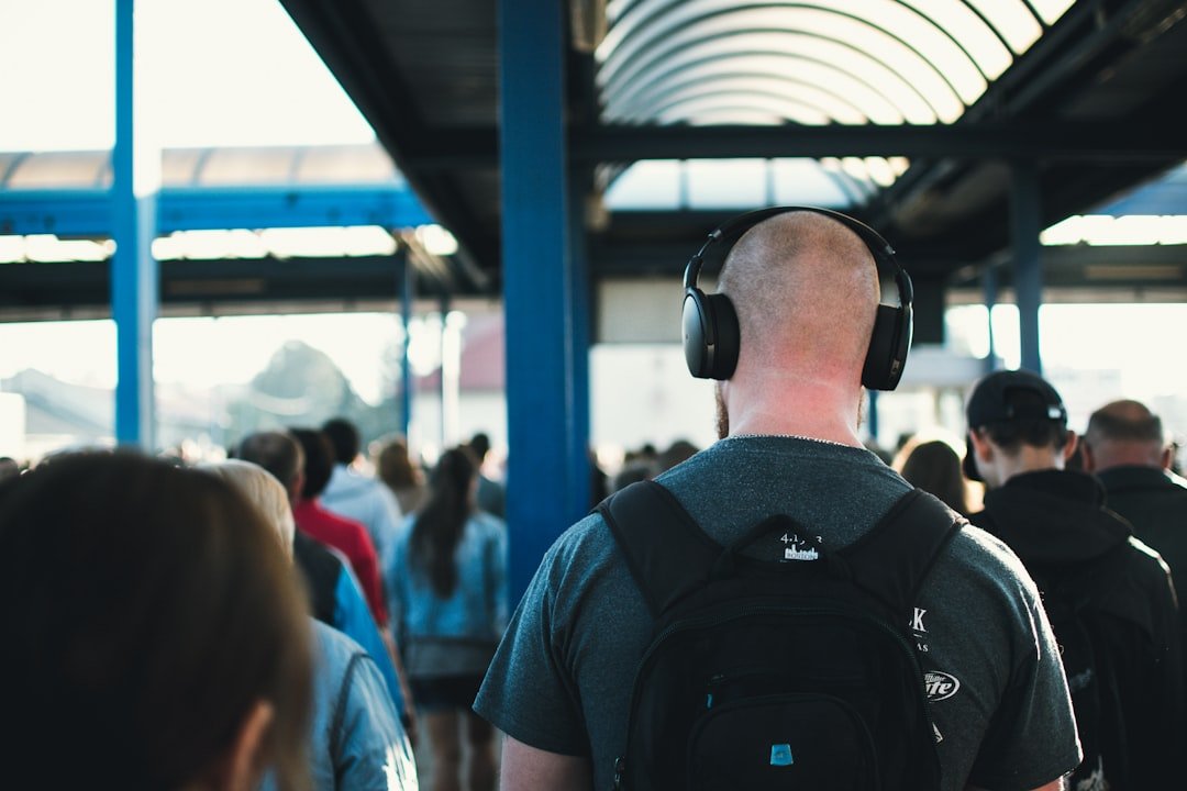 Crowd walking in a transit station, with one person in focus wearing headphones and a backpack.