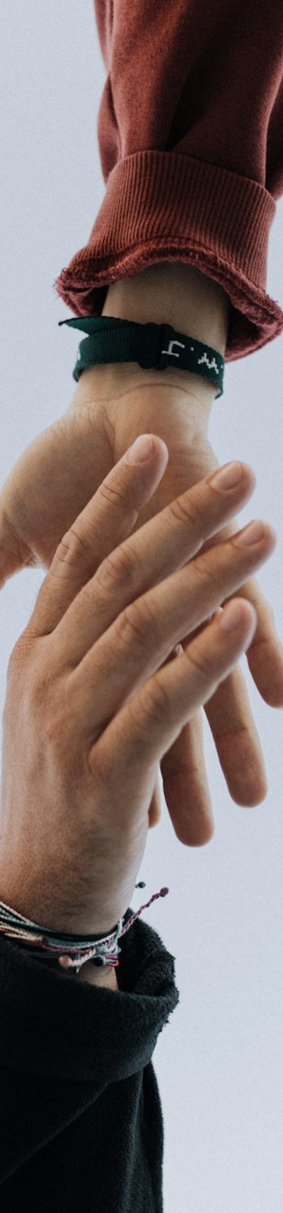 Two hands reaching toward each other, one with a red sleeve and wristband, the other with colorful bracelets.